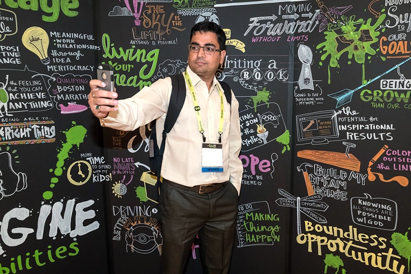 A conference booth attendee takes a selfie against a wall of visual notes